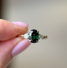 Gold ring with green gemstone held by a hand against a blurred background