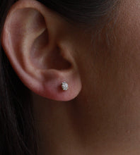 Close-up of an ear wearing a diamond earring with dark hair and skin in the background