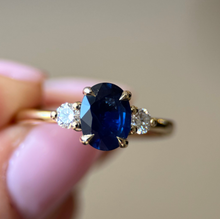 Gold ring with a blue gemstone held by a hand against a blurred background