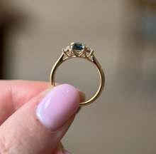 Gold ring with a gemstone held between fingers against a blurred background