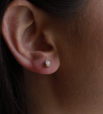 Close-up of an ear wearing a diamond earring with dark hair and skin in the background